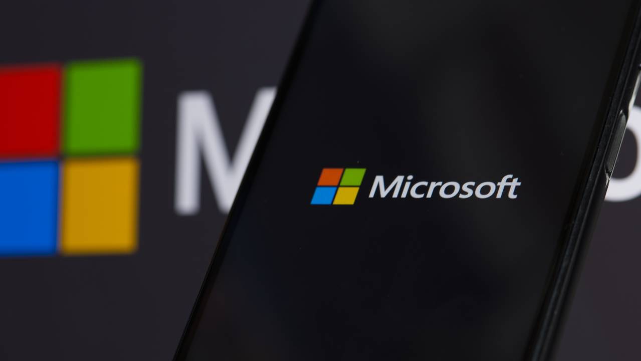 logo microsoft su schermo del cellulare e pc sullo sfondo